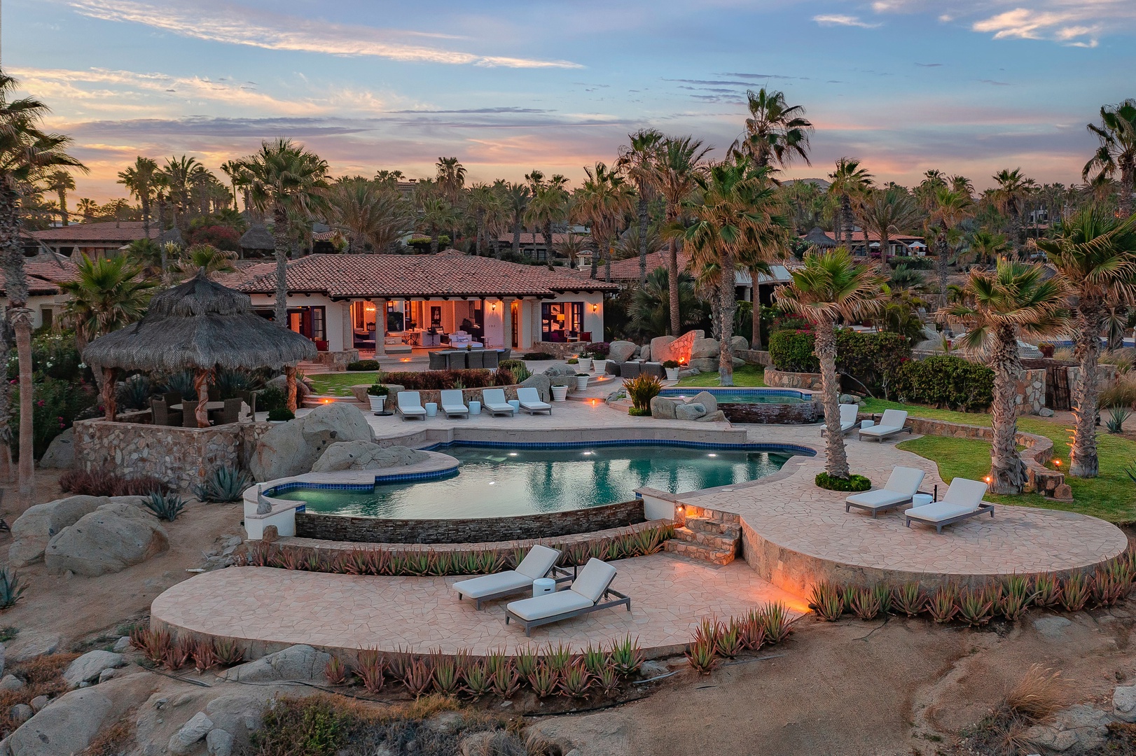 Luxury villa with swimming pool surrounded by tropical landscaping in an upscale resort area during golden hour.