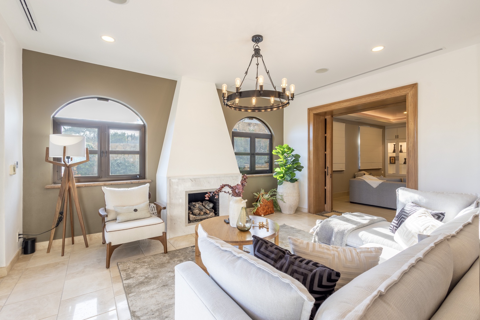 Picture yourself relaxing in this sun-drenched living space with its cozy fireplace, elegant chandelier, and plush seating. The charming arched windows frame natural light, while the open layout flows seamlessly into the bedroom suite—your perfect home aw