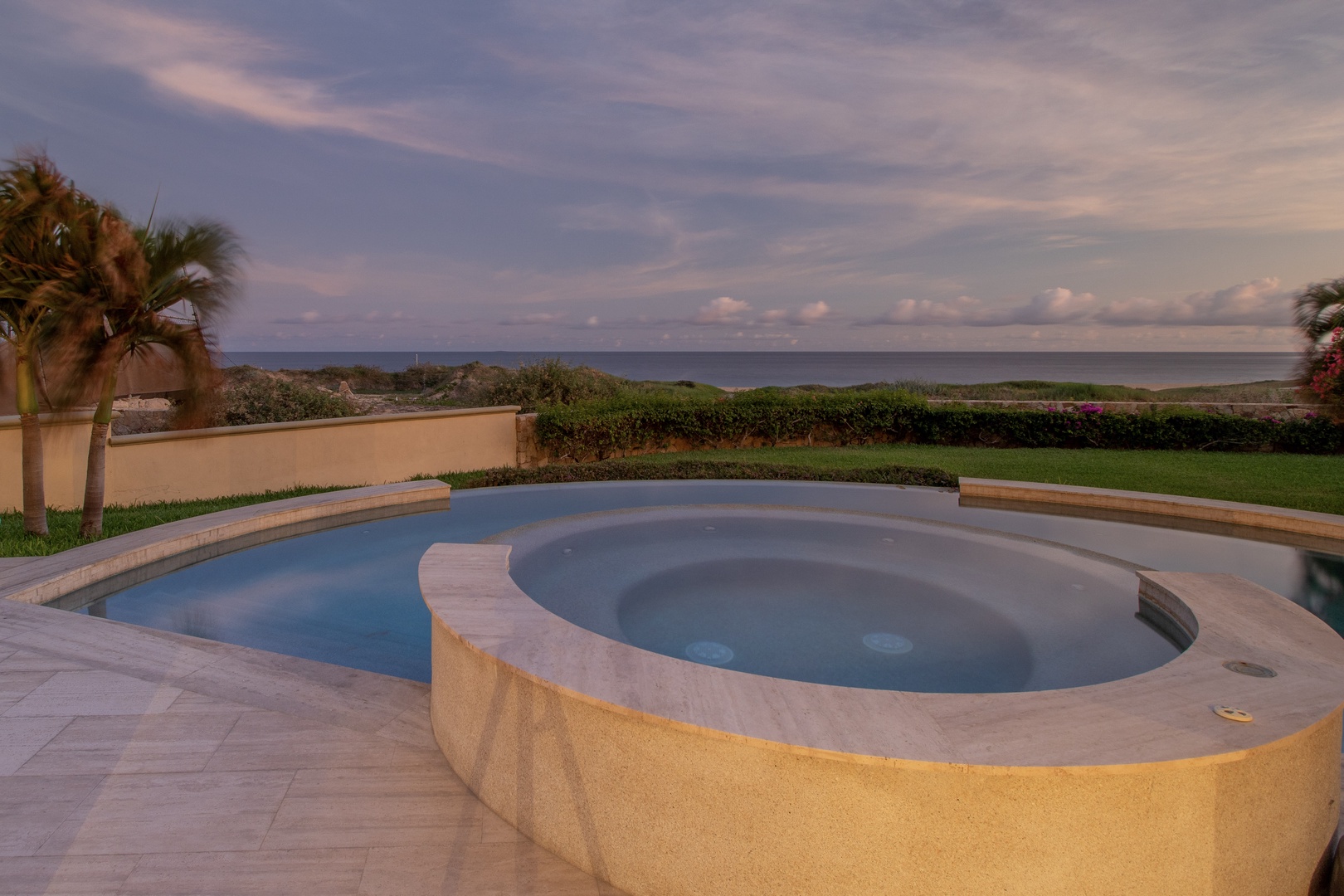 Oceanfront property featuring an elevated hot tub and pool overlooking the sea, framed by tropical palms and manicured lawns along the coastline.
