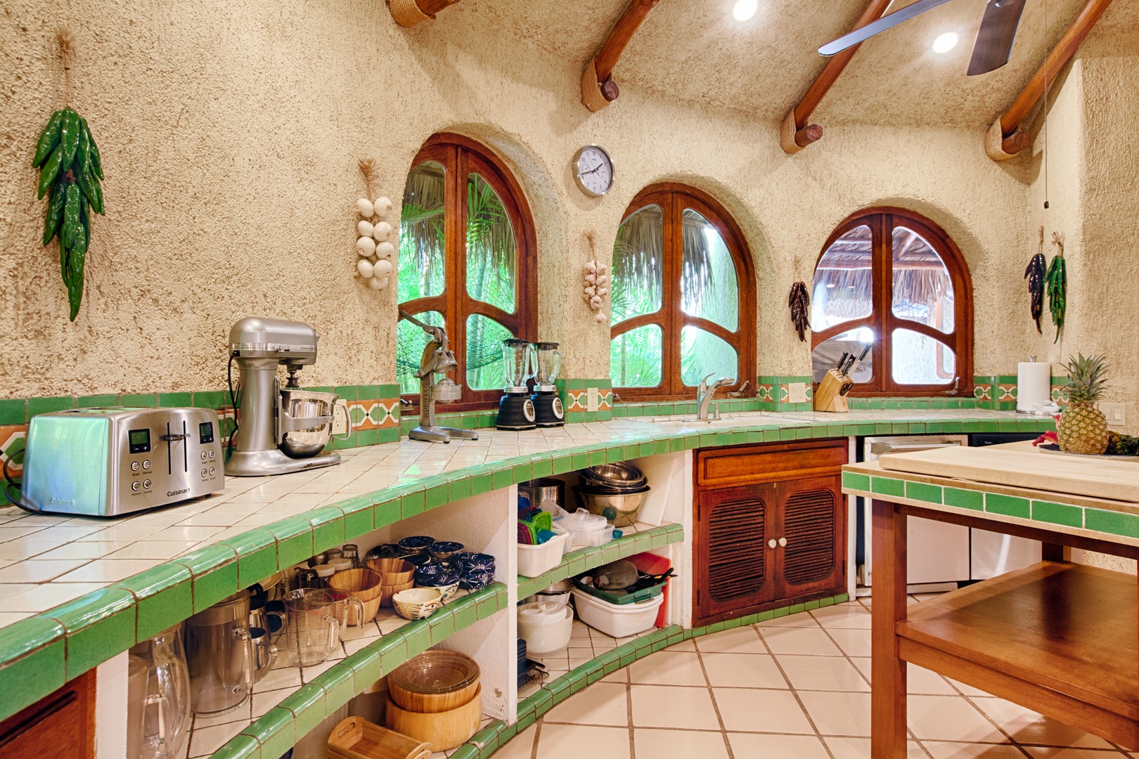 Your charming kitchen features vibrant green tile counters, exposed beams, and garden views through arched windows.