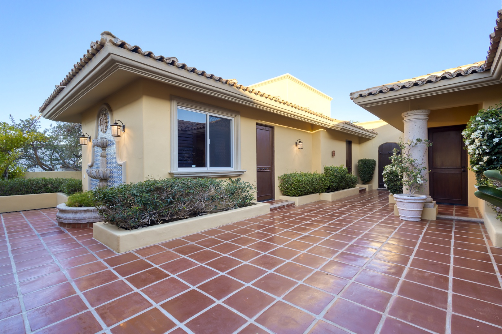 Elegant Mediterranean-style villa exterior showcases warm stucco walls, red tile roofing, and a grand terracotta-tiled courtyard entrance.
