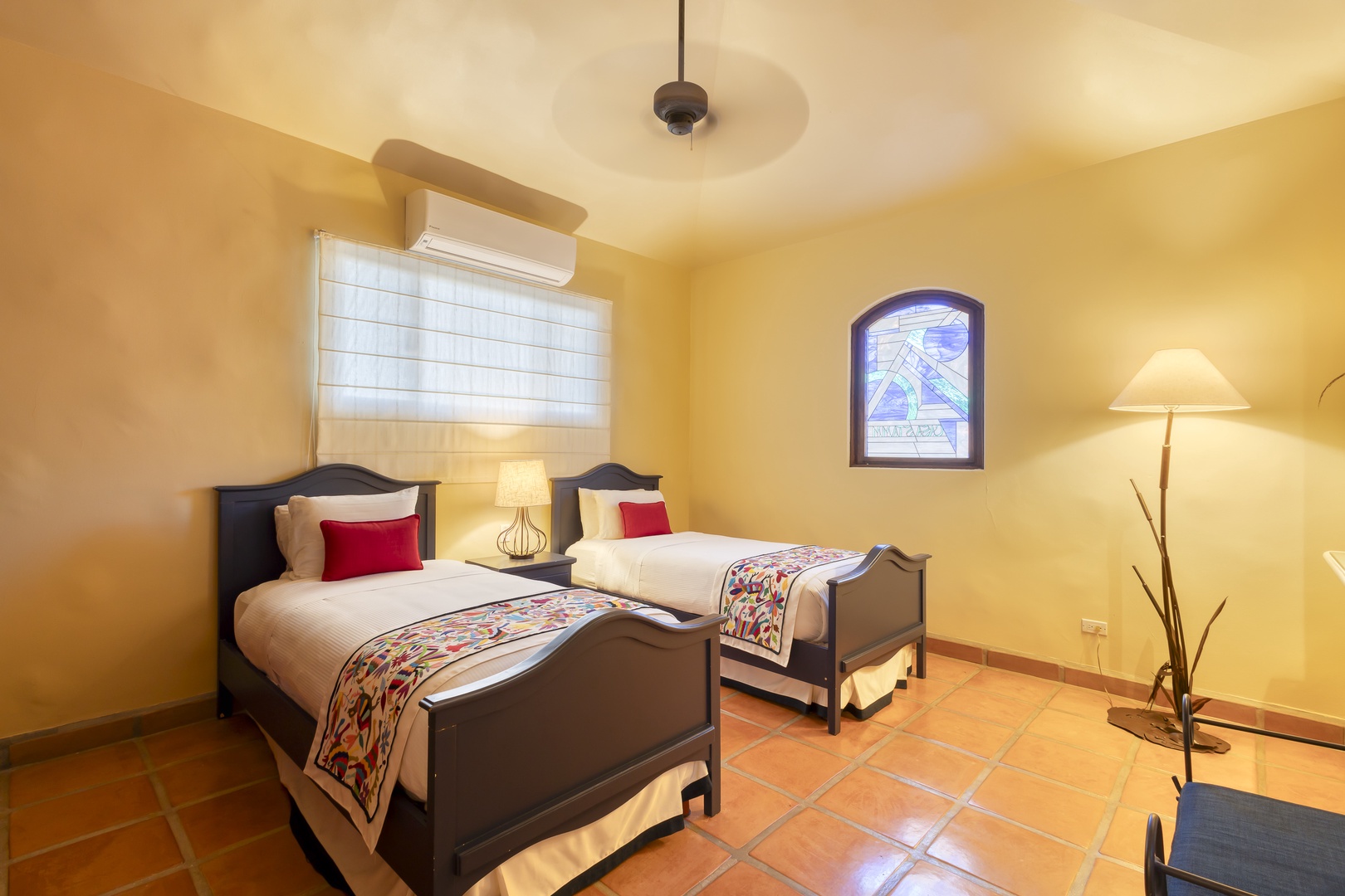Rest peacefully in your cozy twin bedroom with warm yellow walls, comfortable beds adorned with colorful throws, and gentle lighting.