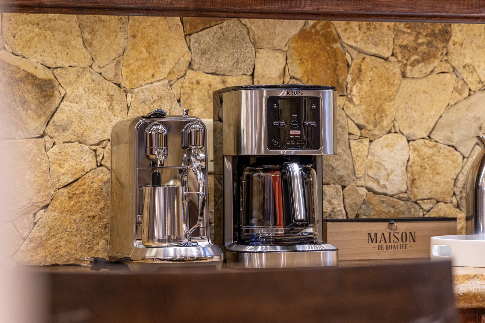 A sleek coffee station awaits your morning ritual, featuring a professional espresso maker and drip coffee machine set against natural stone walls for a perfect start to your day.