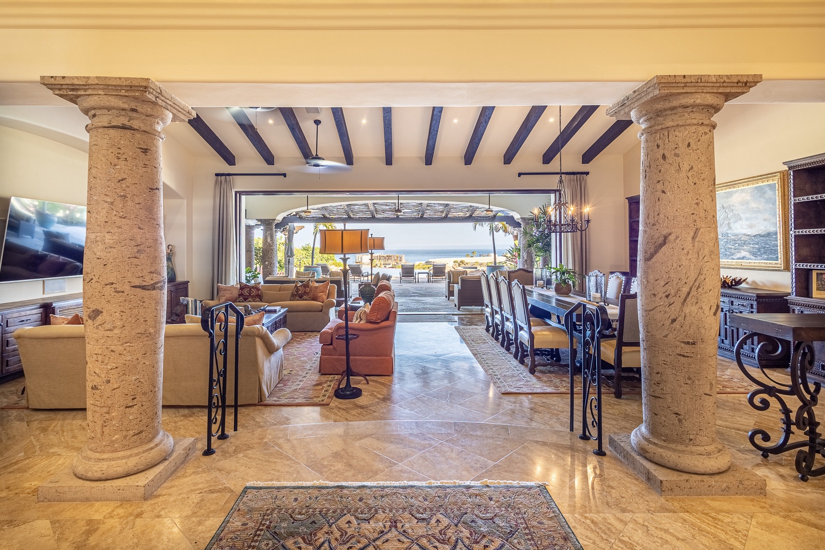 The grand stone columns and exposed wooden beams frame your stunning great room, where a spacious living area flows seamlessly into the elegant dining space and opens to breathtaking ocean views beyond.