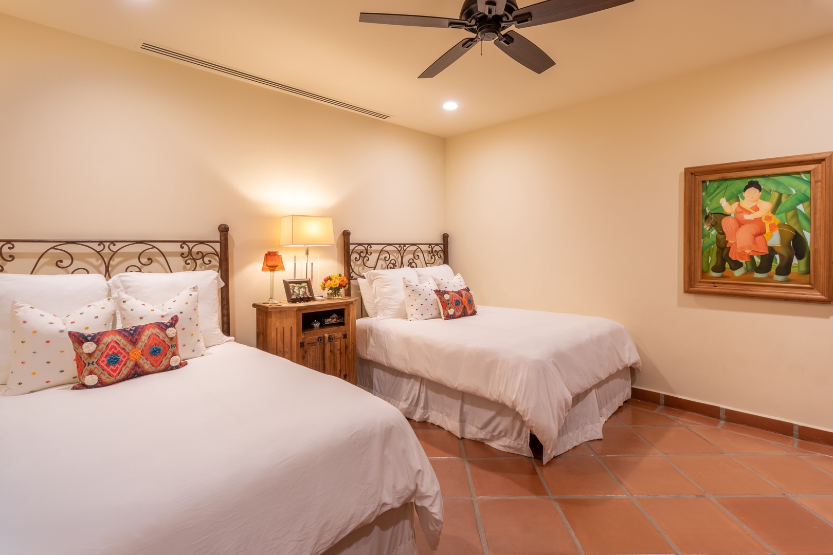 Two plush beds with crisp linens and colorful accent pillows create a cozy haven for restful nights. The ceiling fan and warm lighting add comfort to your stay.