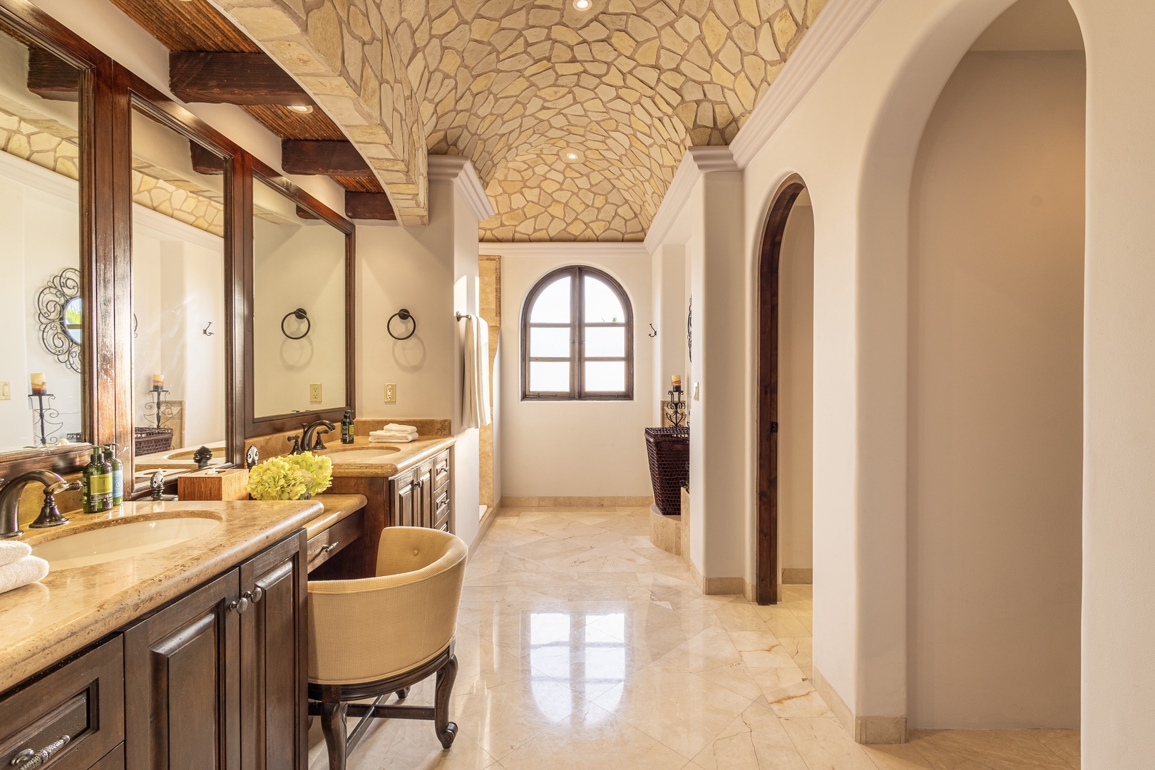This stunning bathroom features a vaulted stone ceiling, dual vanities with granite countertops, and elegant arched doorways that create a spa-like retreat for your relaxation.