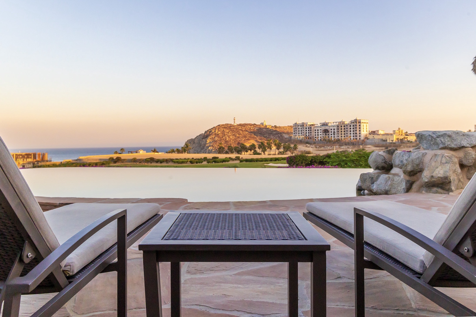 Unwind on the private terrace overlooking a serene lagoon and distant coastal hills, where golden-hour light paints a peaceful waterfront scene.