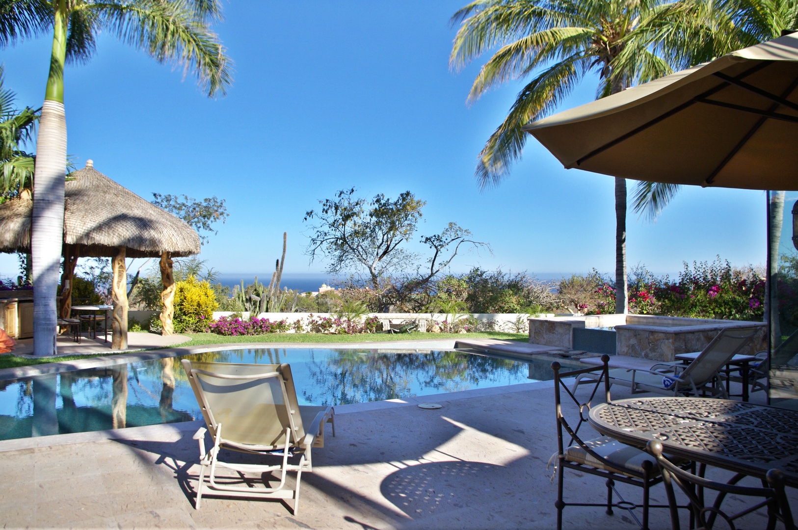 A serene poolside retreat framed by swaying palms and colorful gardens, with sweeping views of the ocean beyond—a perfect tropical escape.