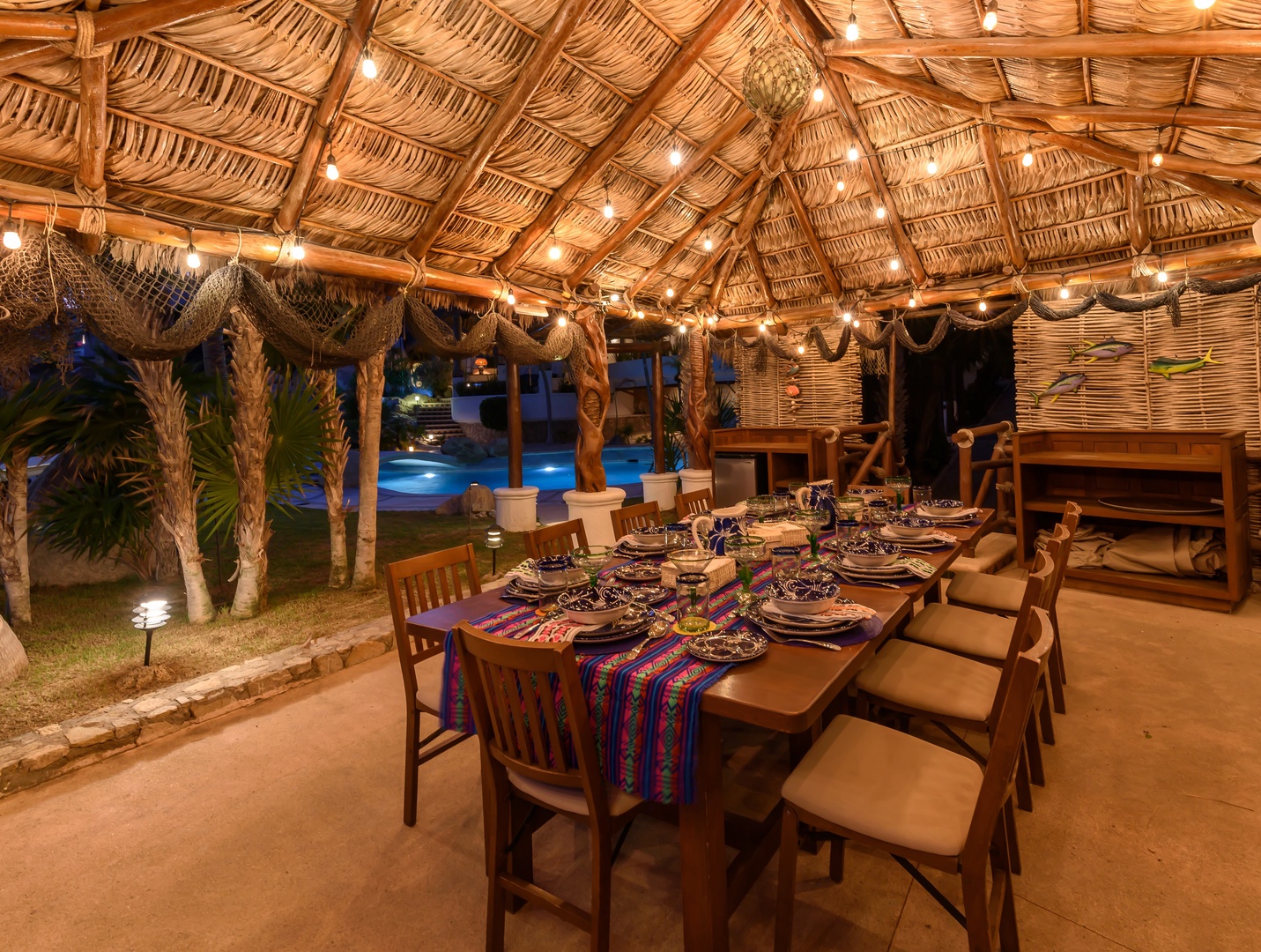 Gather under twinkling lights at your private palapa, where vibrant textiles dress the table and the pool glows just beyond—perfect for memorable evening meals together.