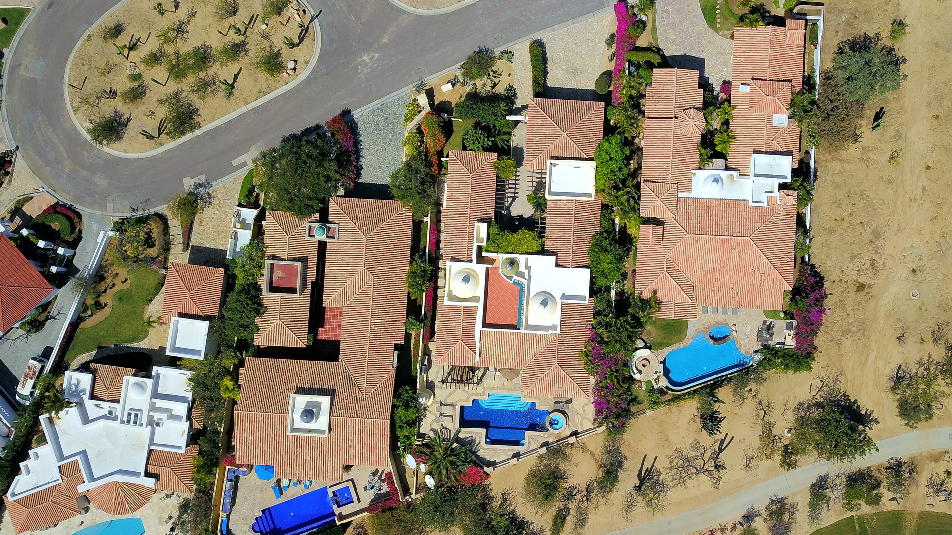 Aerial view of a Mediterranean-style resort complex with terracotta roofs, multiple swimming pools, and lush landscaping set in natural surroundings.