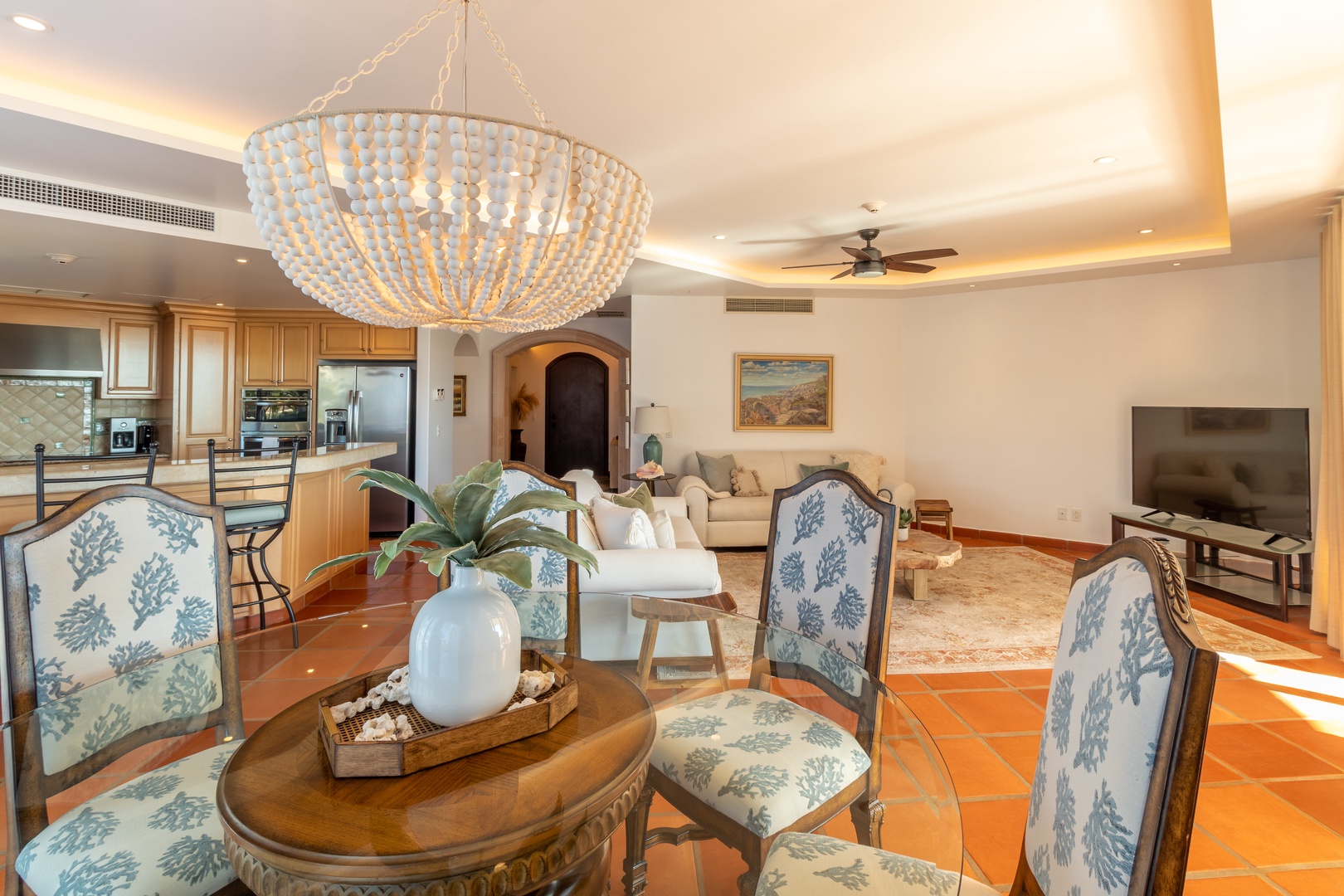 Relax in your open-concept living space, where coastal elegance meets comfort. Sunlight pours over terra cotta floors, beaded chandelier, and inviting seating—perfect for unwinding after beach days.