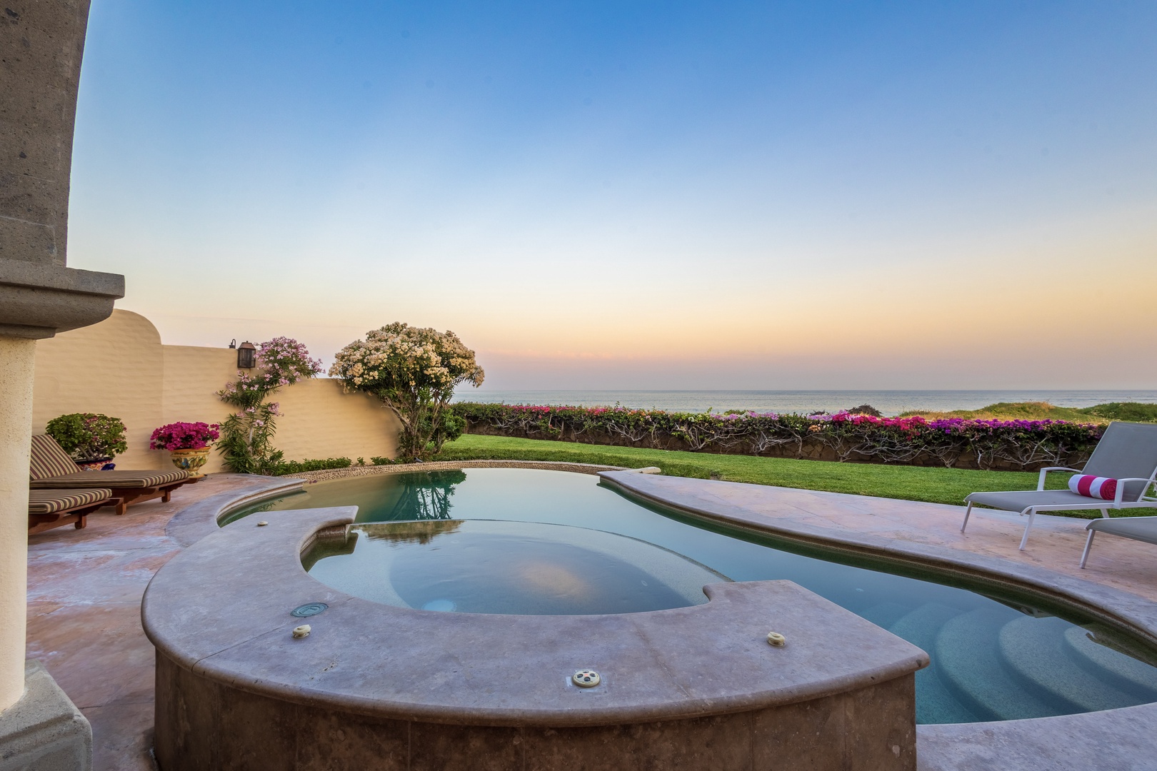 Oceanfront pool and hot tub with manicured gardens, lounge chairs, and sweeping coastal views at sunset. A serene setting for your tropical escape.