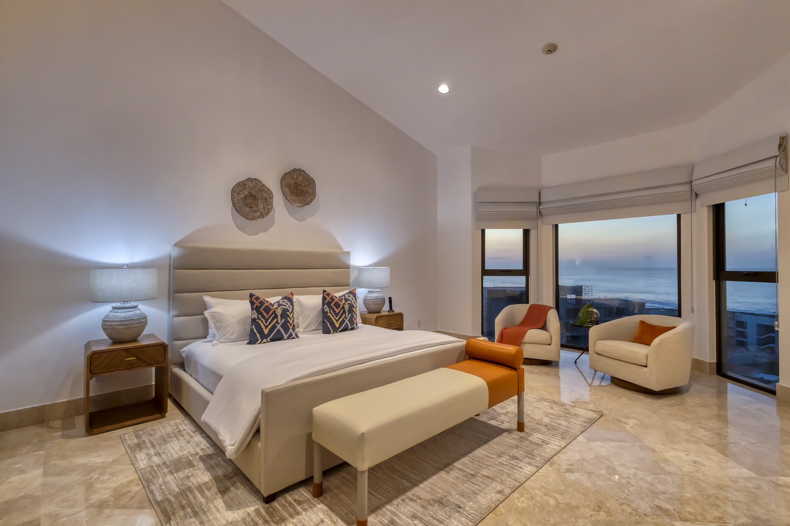 Your elegant bedroom features a plush king bed, stylish seating area, and floor-to-ceiling windows opening to stunning ocean views—perfect for waking up to sunrise over the waves.