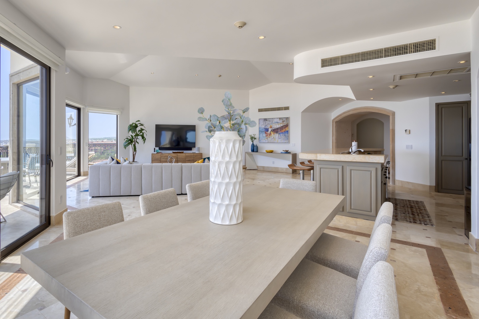 This bright, airy space blends dining and living seamlessly. Natural light pours through glass doors, revealing coastal views, while soft textures and elegant arches invite you to relax and savor every moment here.