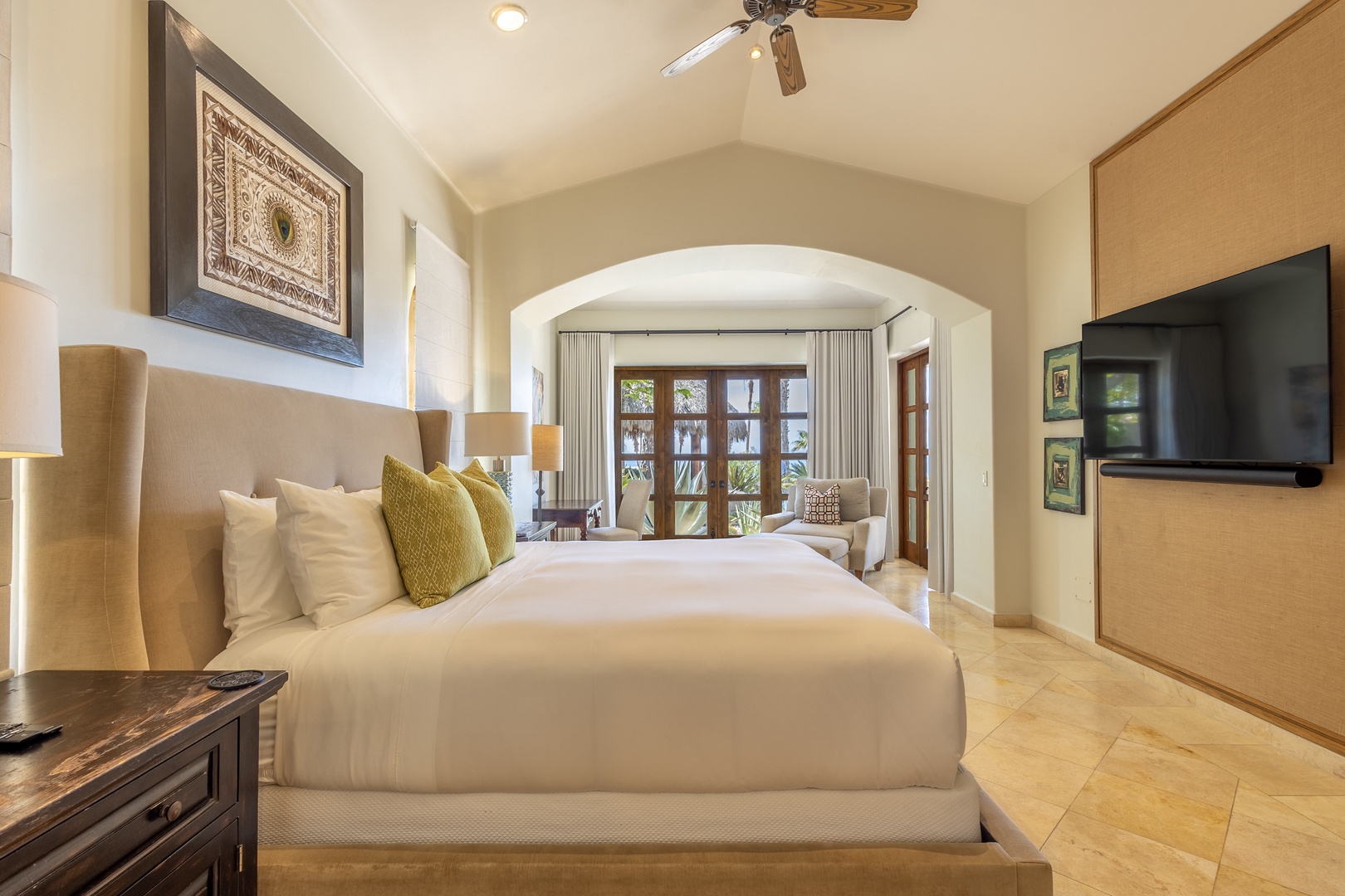 Sink into crisp white linens and let the gentle ceiling fan cool you as natural light streams through elegant French doors in your serene bedroom retreat.