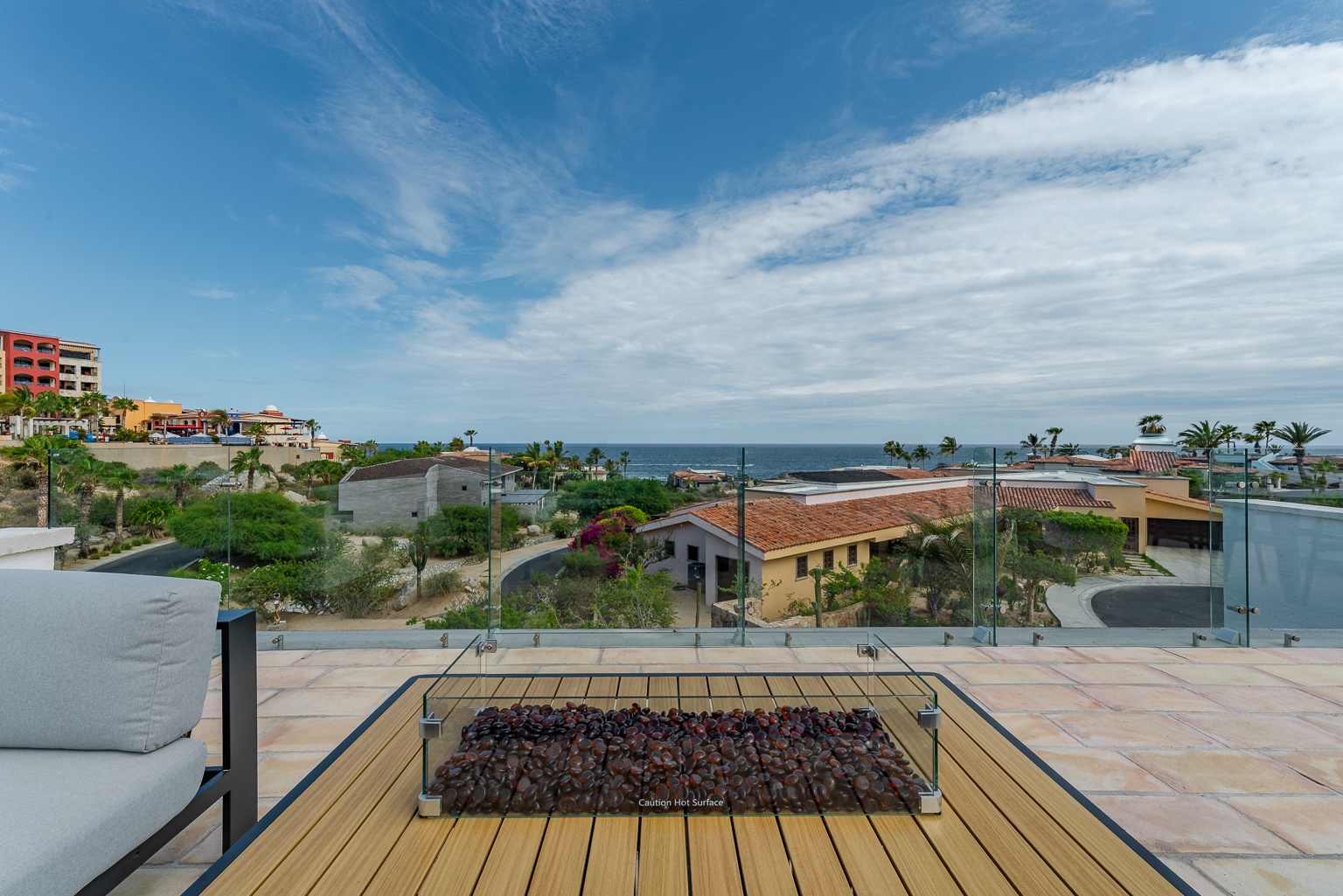 A rooftop terrace offers sweeping coastal views across the neighborhood to the sparkling ocean. The glass-enclosed fire pit provides a perfect gathering spot for relaxing under open skies.