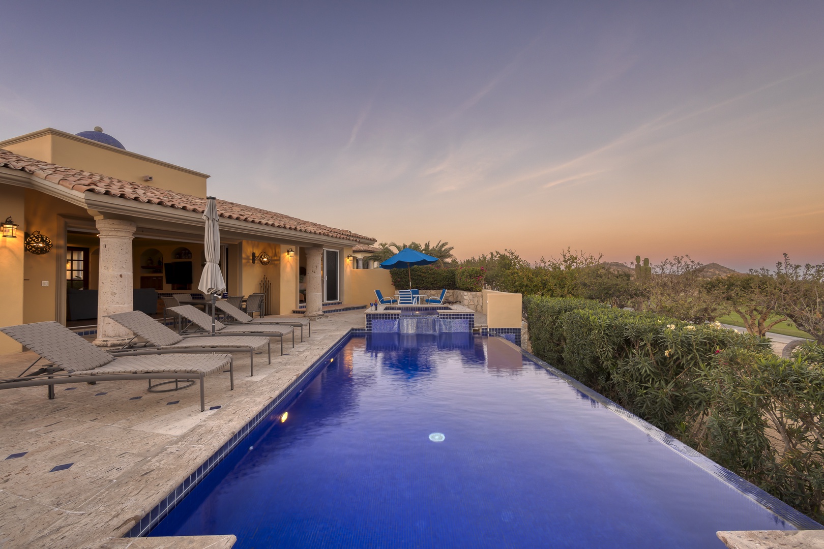 Mediterranean-style villa with sparkling pool at sunset, surrounded by desert landscape and mountain views.