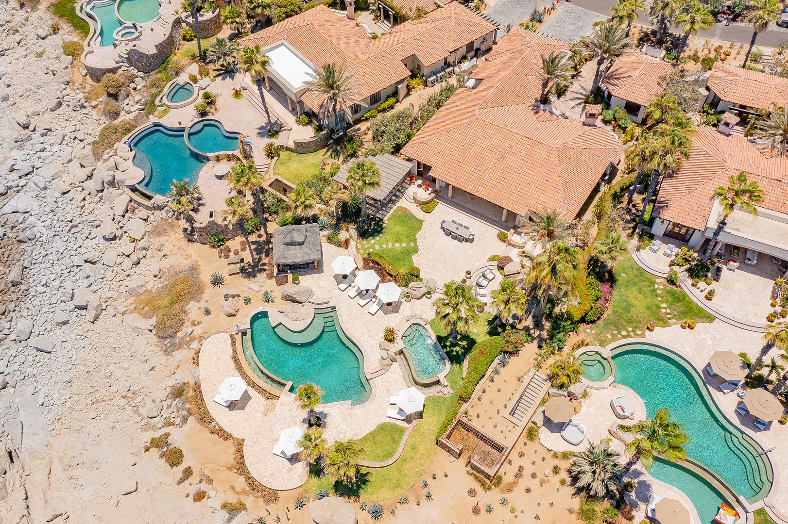 Stunning aerial view of a luxurious beachfront resort featuring multiple swimming pools, tropical landscaping, and elegant villa-style accommodations with terracotta rooftops.