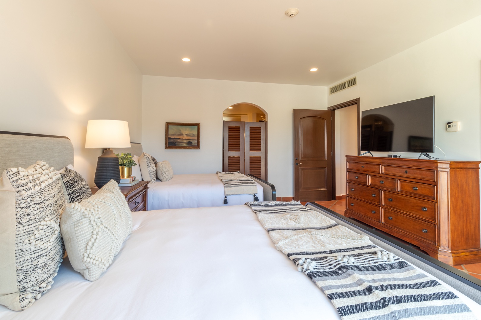 Sink into plush beds topped with cozy textured pillows and soft throws, all bathed in warm lamplight. Your serene bedroom invites peaceful nights with wood furnishings and a calming neutral palette.