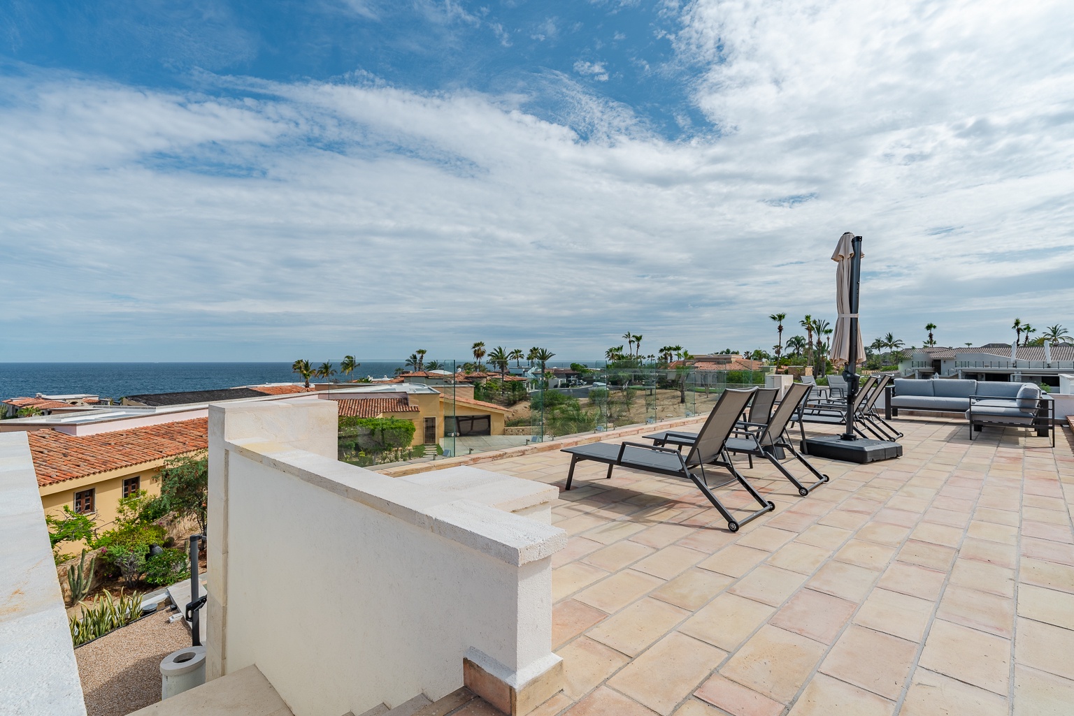 A rooftop terrace offers sweeping coastal views overlooking nearby vacation homes, tropical palms, and the endless ocean horizon—an elevated vantage point at this seaside property.
