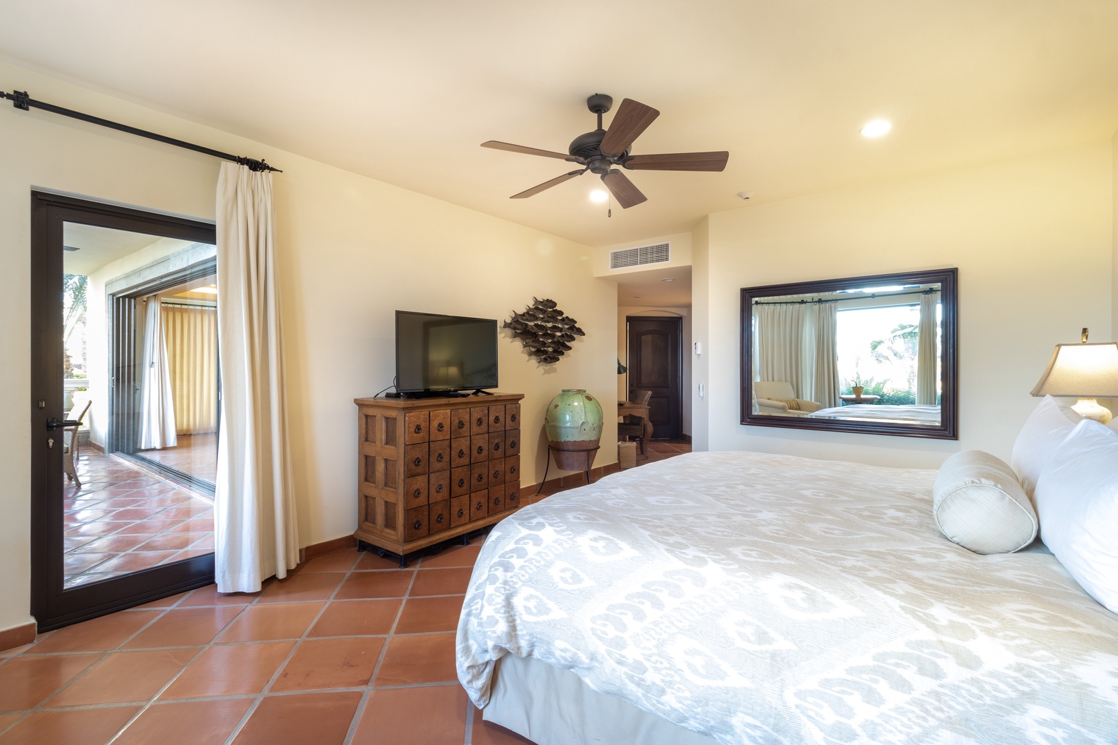 Unwind in your serene bedroom with terracotta tile floors, vaulted ceilings, and a ceiling fan to keep you cool. The elegant wood dresser and TV make your stay effortlessly comfortable.