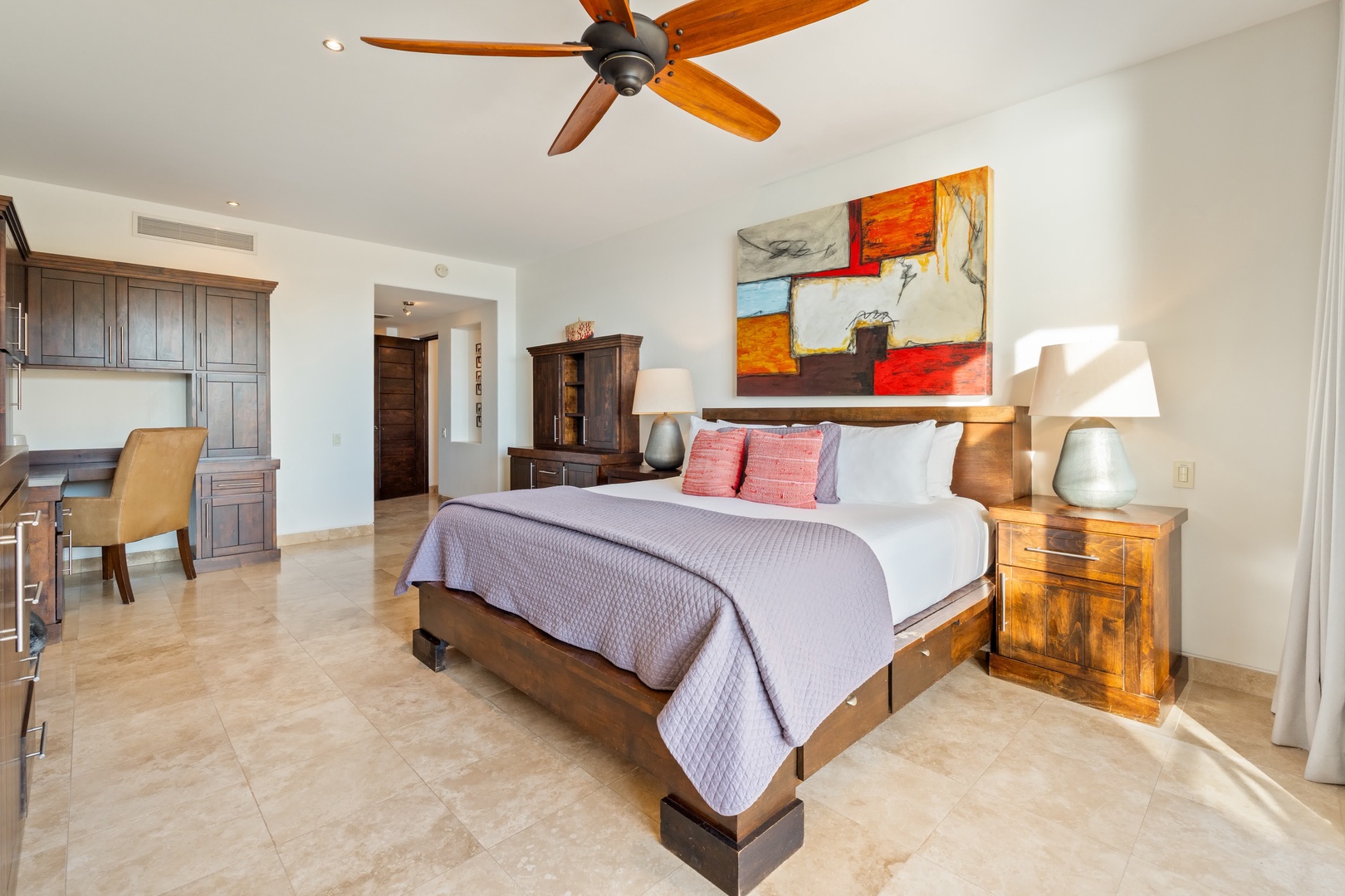 Rest peacefully in your spacious suite featuring rich wood furniture, colorful artwork, and a ceiling fan for perfect comfort.