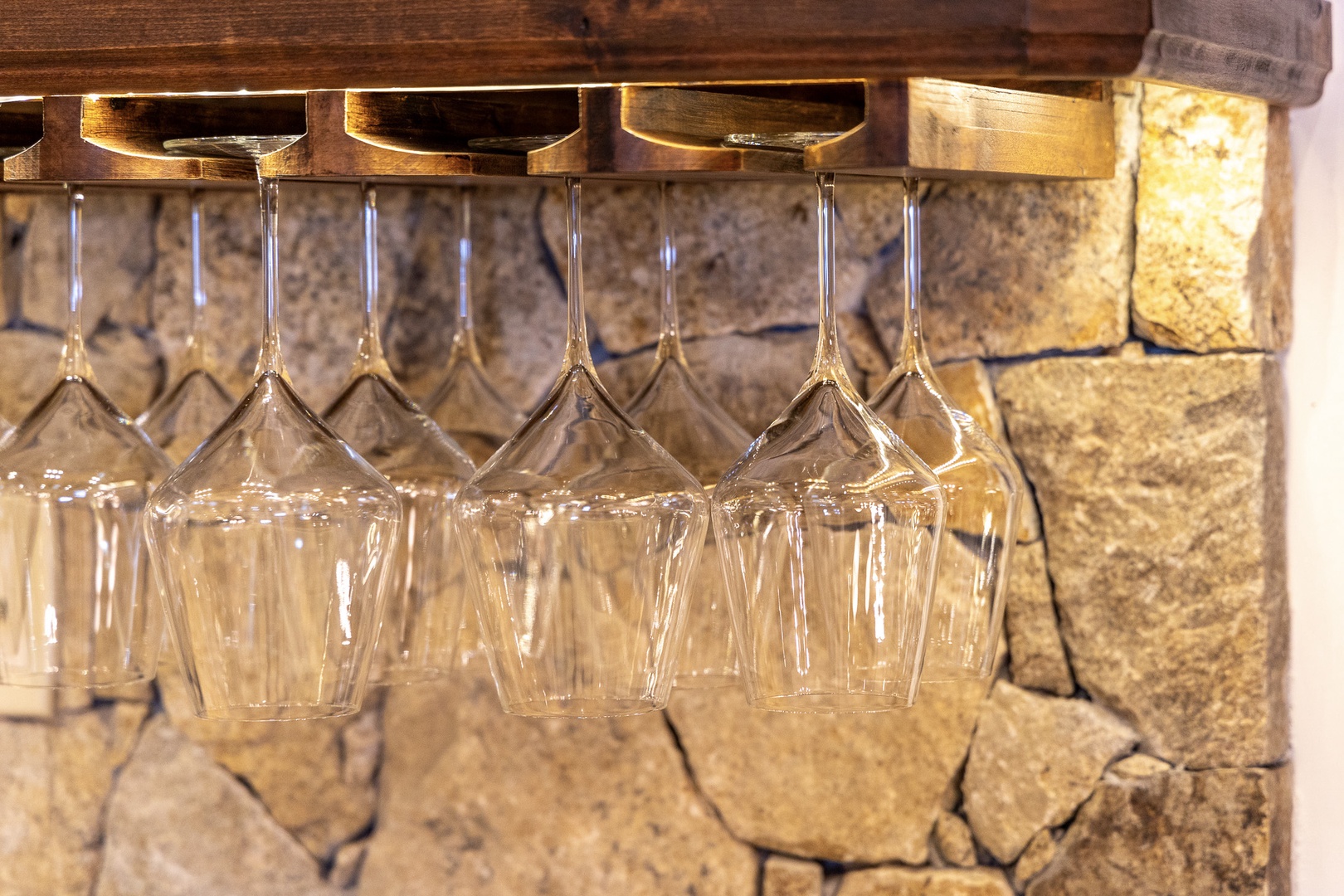 Rustic wooden wine glass rack awaits your favorite bottles. The stone wall and warm wood create a charming, homey atmosphere—perfect for cozy evenings in.