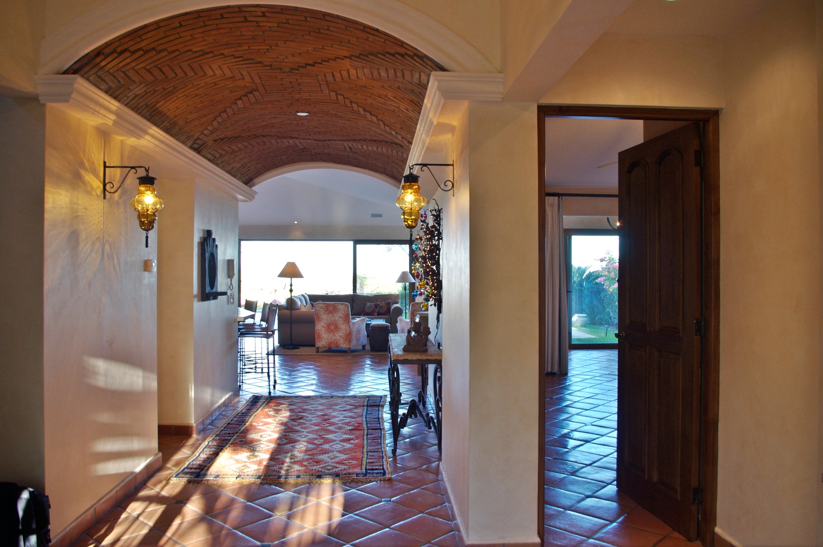 Step through the arched entrance into your warm, sun-drenched hallway where rustic terracotta tiles and glowing lanterns guide you toward the inviting living space beyond.