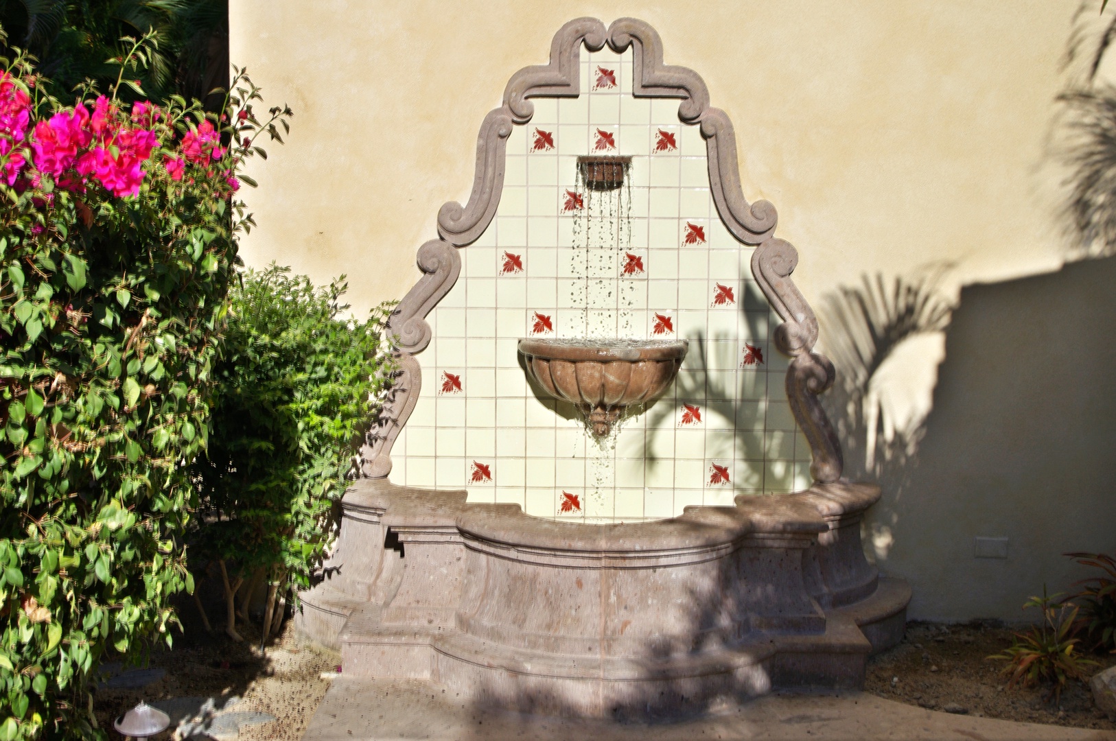 A charming Spanish-style tiled fountain adorned with vibrant pink bougainvillea creates a serene focal point in your private outdoor garden retreat.