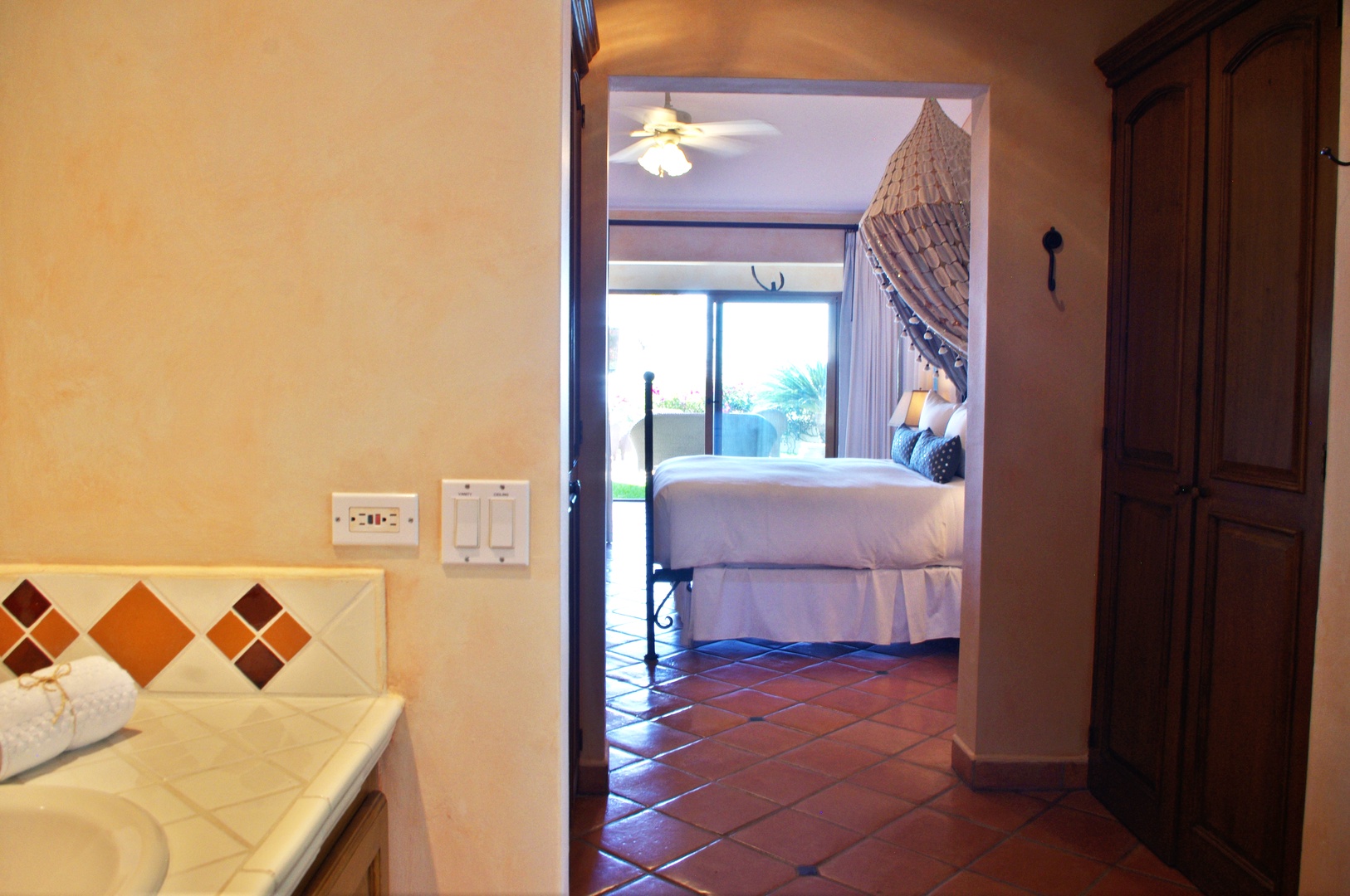Step into your peaceful retreat where warm terracotta tiles guide you to a sunlit bedroom with tropical breezes and soothing ceiling fan overhead.