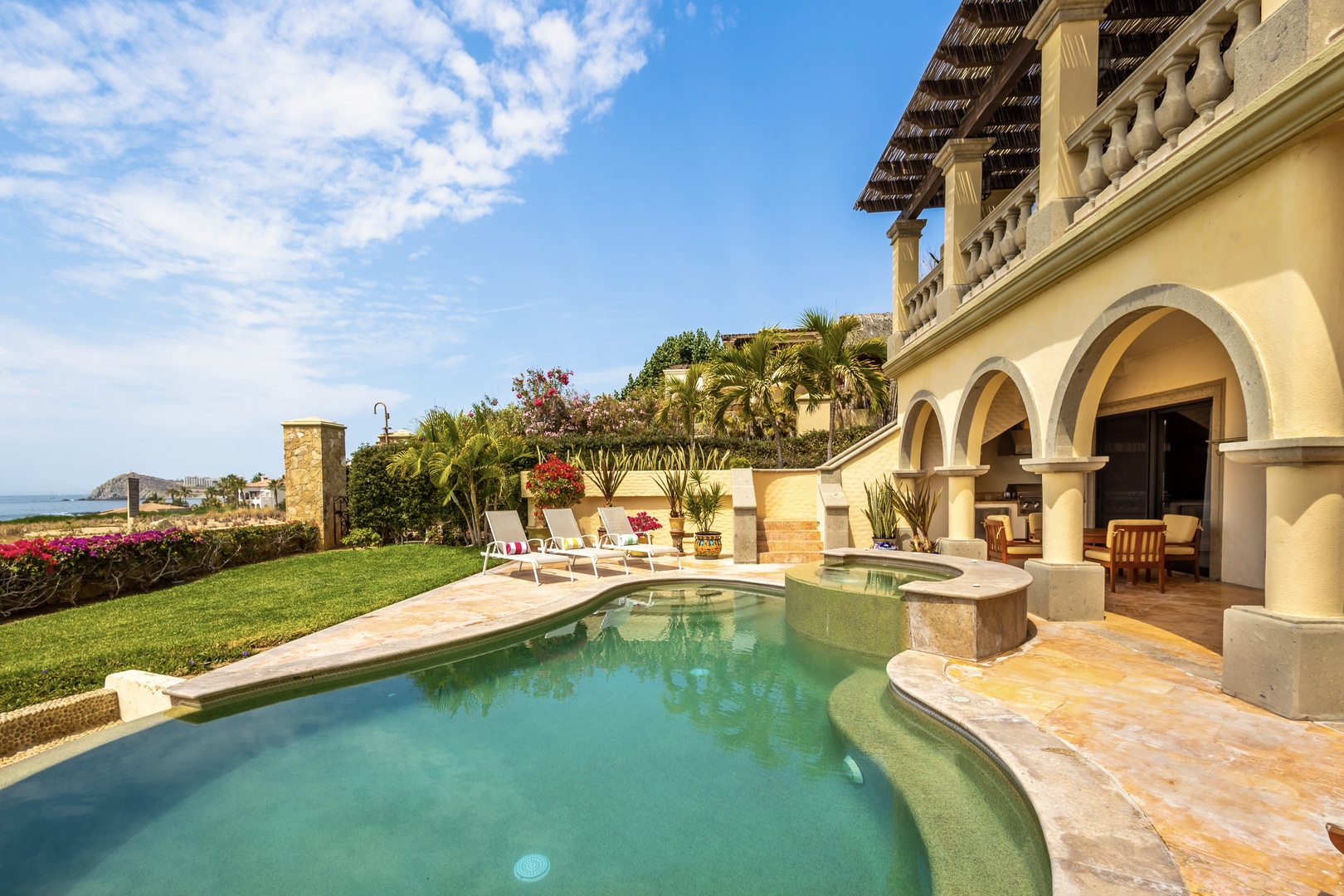 A stunning beachfront villa with Spanish colonial architecture nestled on Mexico's Pacific coast, featuring a private curved pool, manicured lawns, and sweeping ocean views.