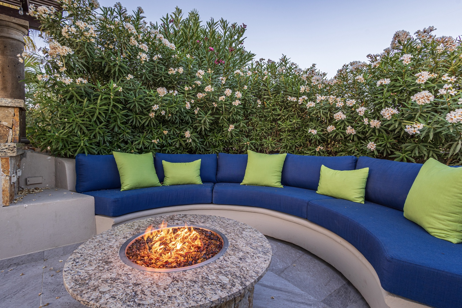 Gather around the fire in this cozy outdoor lounge, where vibrant cushions and lush greenery create your perfect evening retreat under open skies.