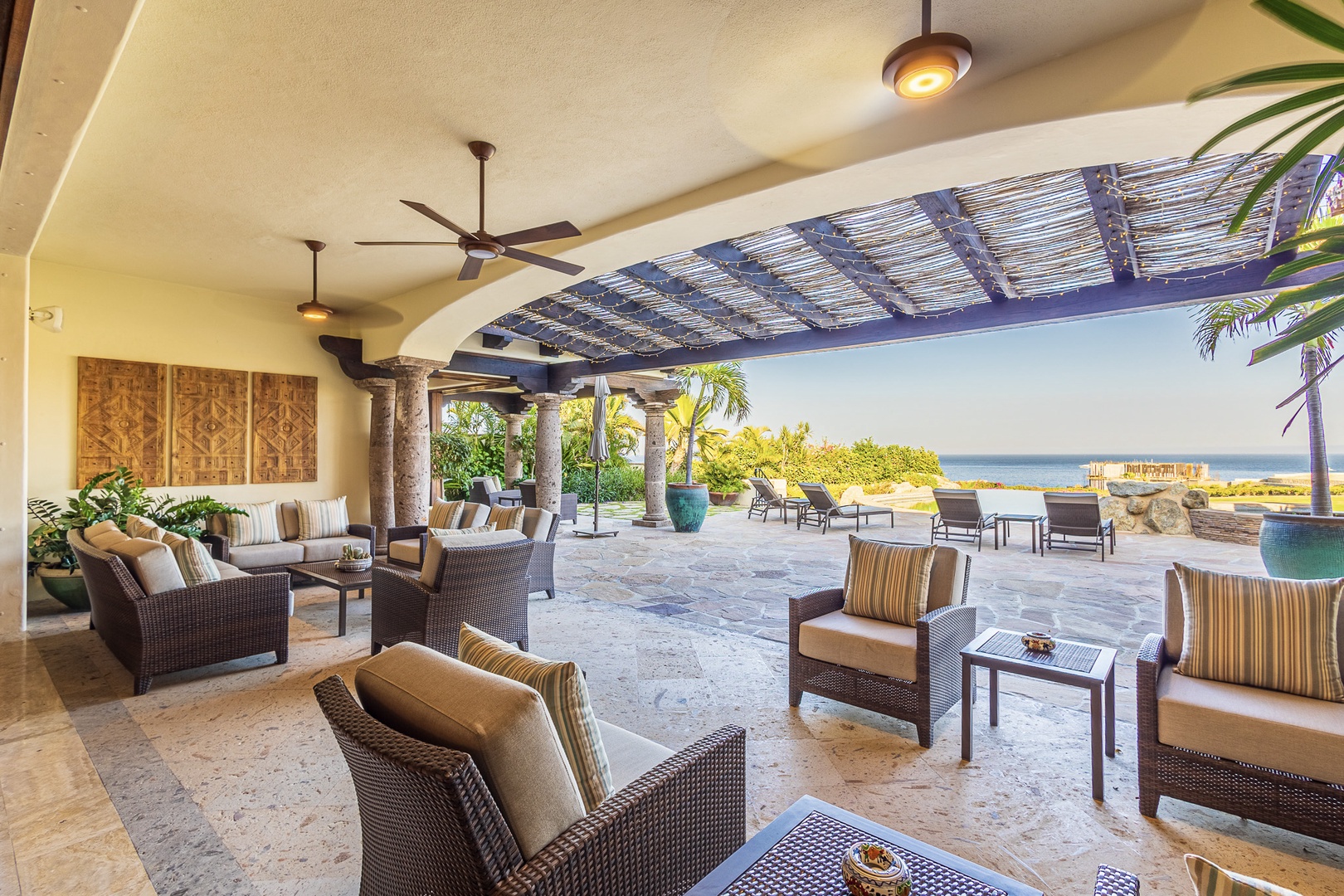 A stunning covered patio with wicker seating, ceiling fans, and sweeping ocean views—perfect for outdoor relaxation and entertainment in a tropical paradise.