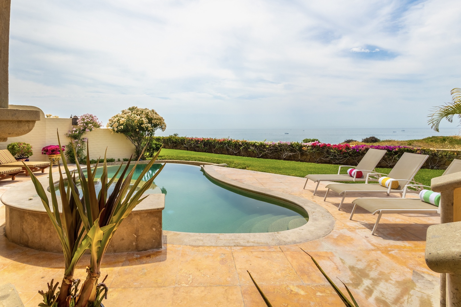Private oceanfront pool with lush gardens and colorful loungers awaits your sun-soaked escape, where manicured lawns meet tranquil waters and endless blue horizons.