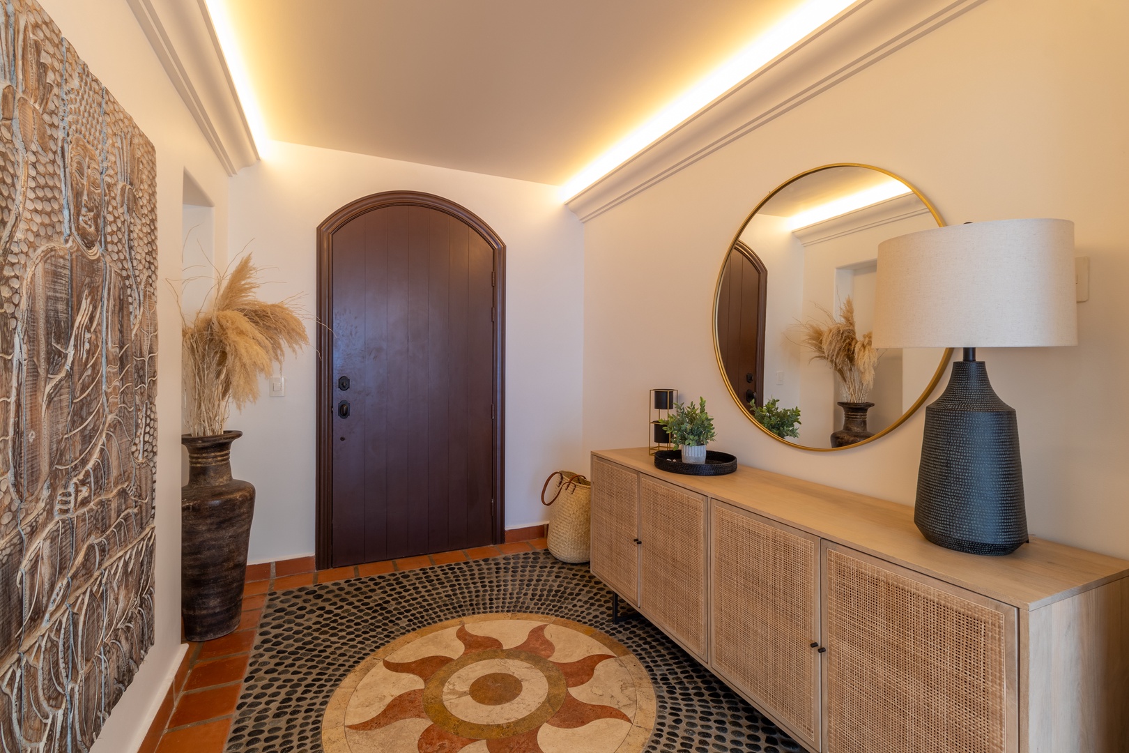 This elegant entryway welcomes you with warm ambient lighting, a striking sunburst mosaic floor, and coastal touches like pampas grass that set a relaxed, inviting tone from the moment you arrive.