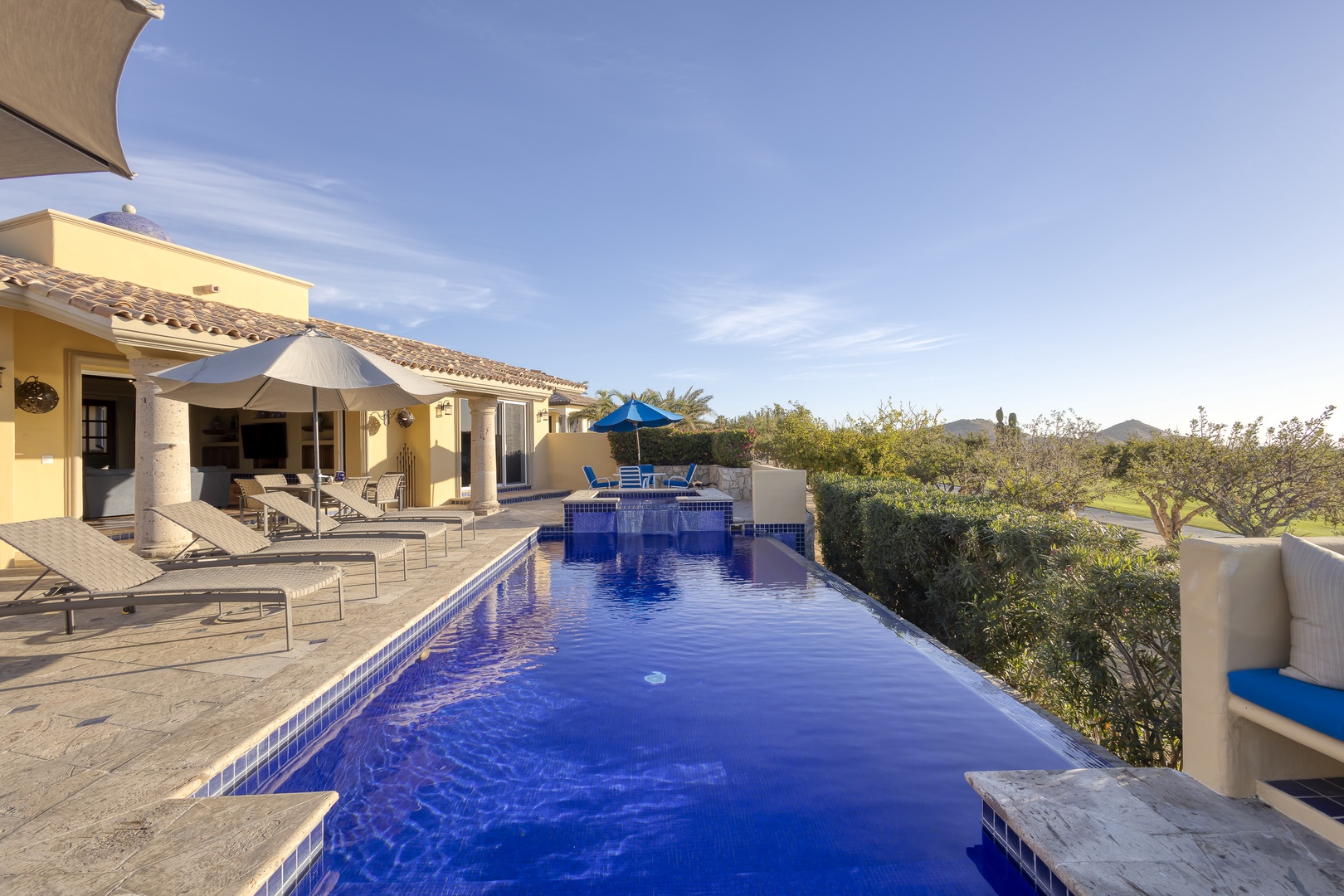 Stunning villa property with infinity pool overlooking lush countryside and mountains under clear blue skies.