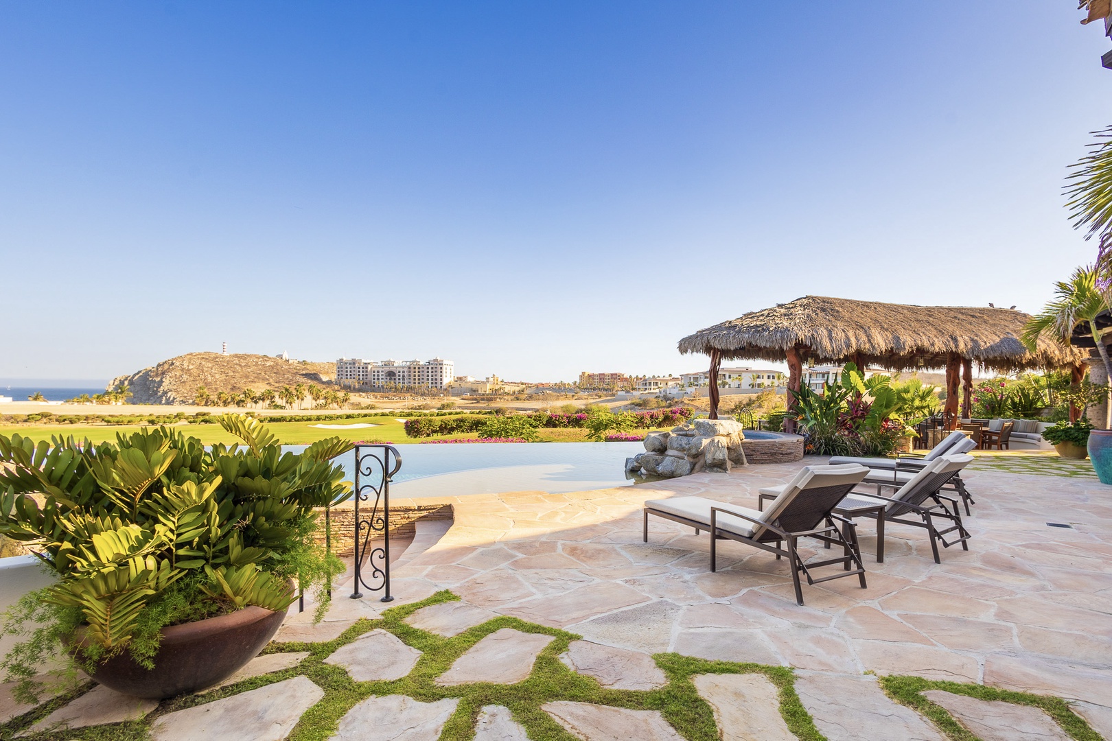 This resort features a private pool area with golf course and ocean views, surrounded by tropical gardens and a thatched palapa for shade.