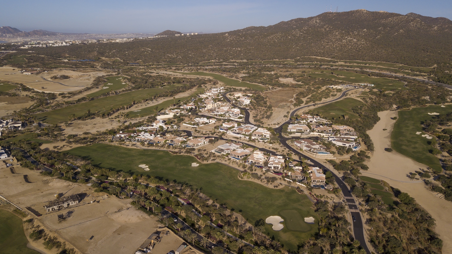 Aerial view of a luxury golf resort community nestled among rolling hills and mountain landscapes in a scenic valley setting.