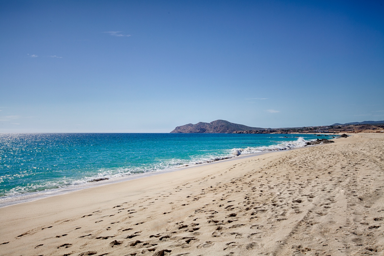 Pristine sandy beach with crystal-clear turquoise waters and dramatic mountain backdrop creates an idyllic coastal escape.