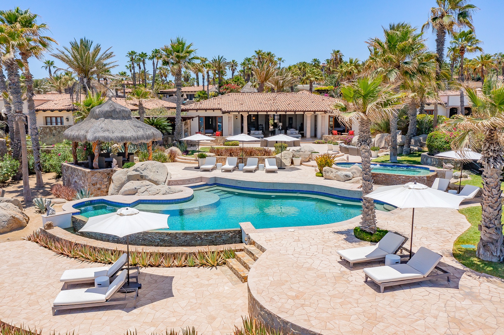 This stunning resort-style property features an expansive pool area with tropical landscaping and multiple buildings situated among lush palm trees.