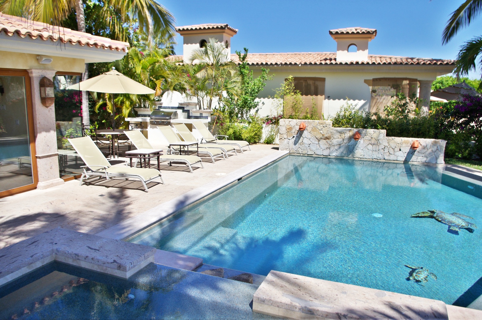 Stunning Spanish-style villa featuring a private pool with water features surrounded by lush palms and vibrant gardens under a brilliant blue sky—your perfect tropical escape.