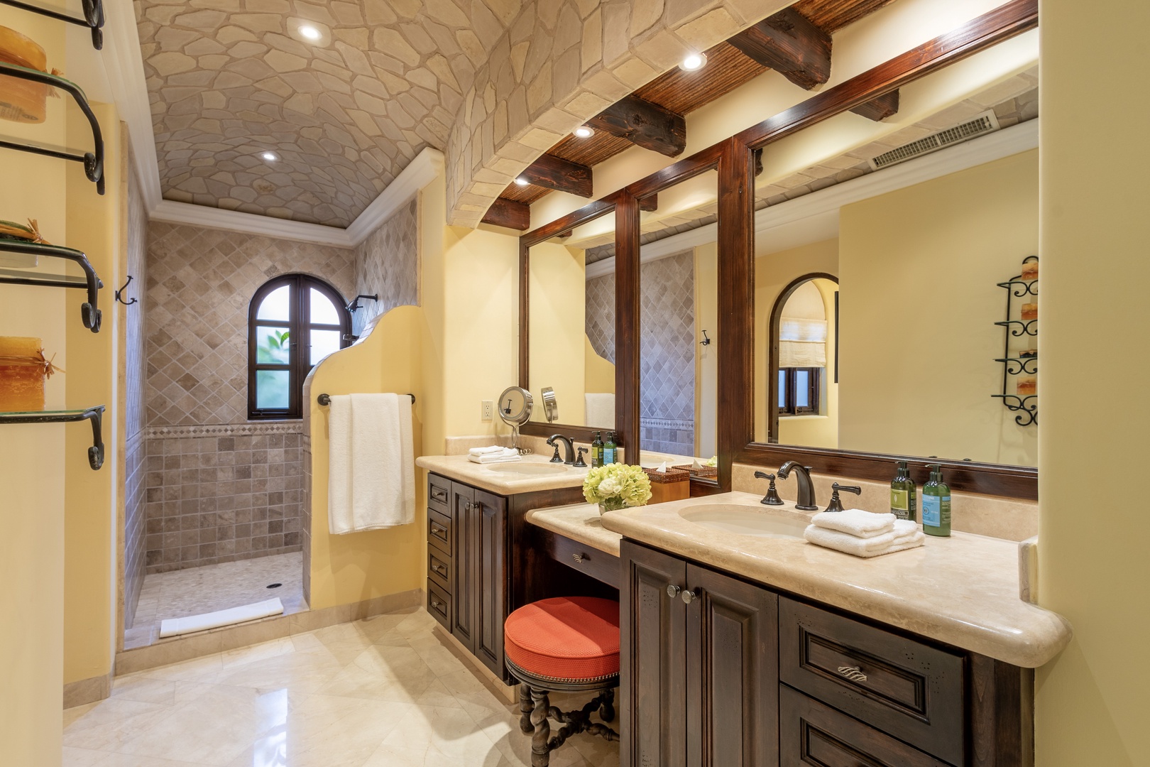Your private bathroom features dual vanities, a walk-in stone shower, rustic wooden beams, and Mediterranean-inspired tile work, combining warmth with elegance for your comfort.