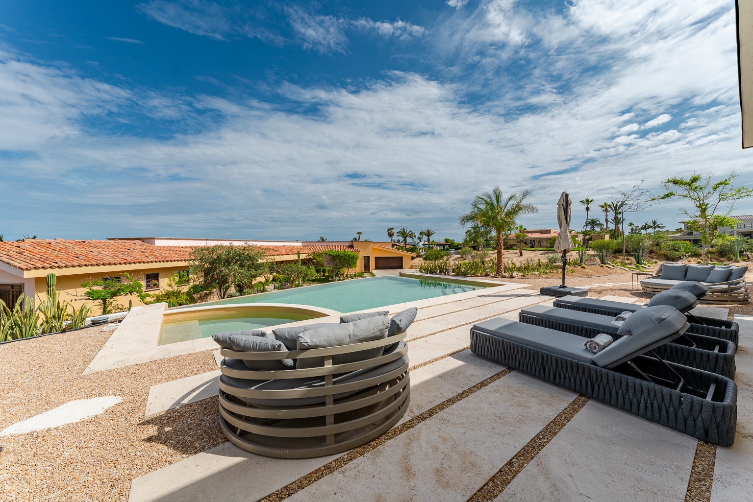 Modern poolside lounging awaits with plush sunbeds and sleek seating, all framed by swaying palms and endless desert sky.