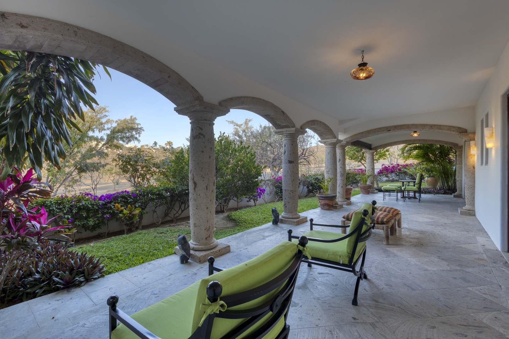 Relax in your elegant covered terrace with stunning stone arches, where lush gardens and tropical blooms create your perfect retreat.