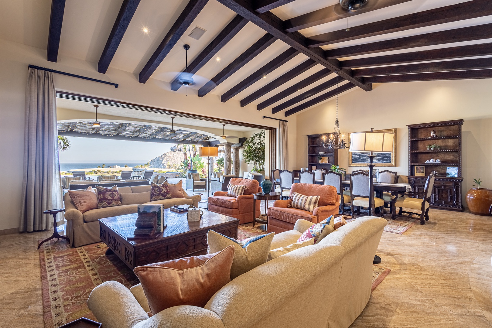 Sink into plush seating beneath dramatic wood-beam ceilings as you gaze toward the sparkling sea. This open-concept living and dining area invites you to unwind in style, with elegant furnishings and coastal breezes just steps away.