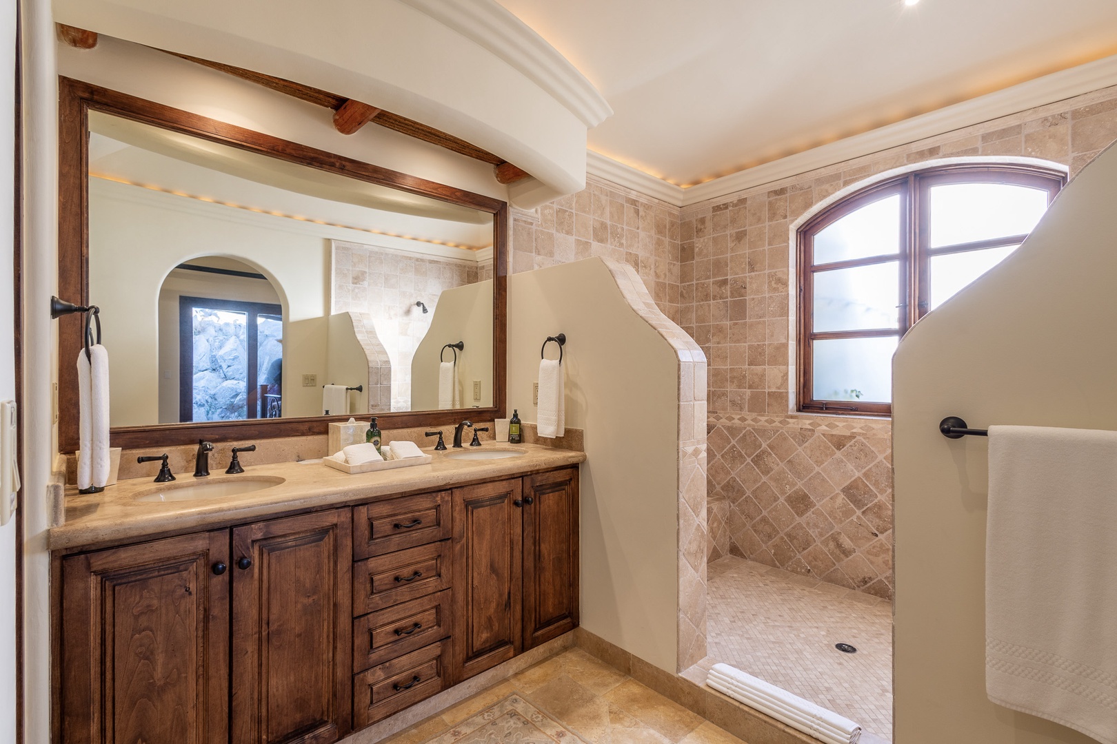 Step into your private bathroom retreat with a spacious walk-in shower, elegant double vanity, and charming arched window that brings in natural light.