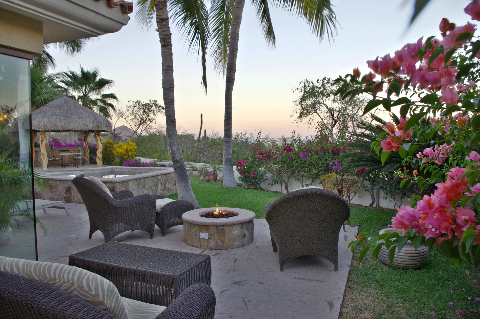 Beautiful outdoor lounge area with tropical gardens, fire pit, and palm trees overlooking a serene landscape—a perfect spot for evening gatherings.