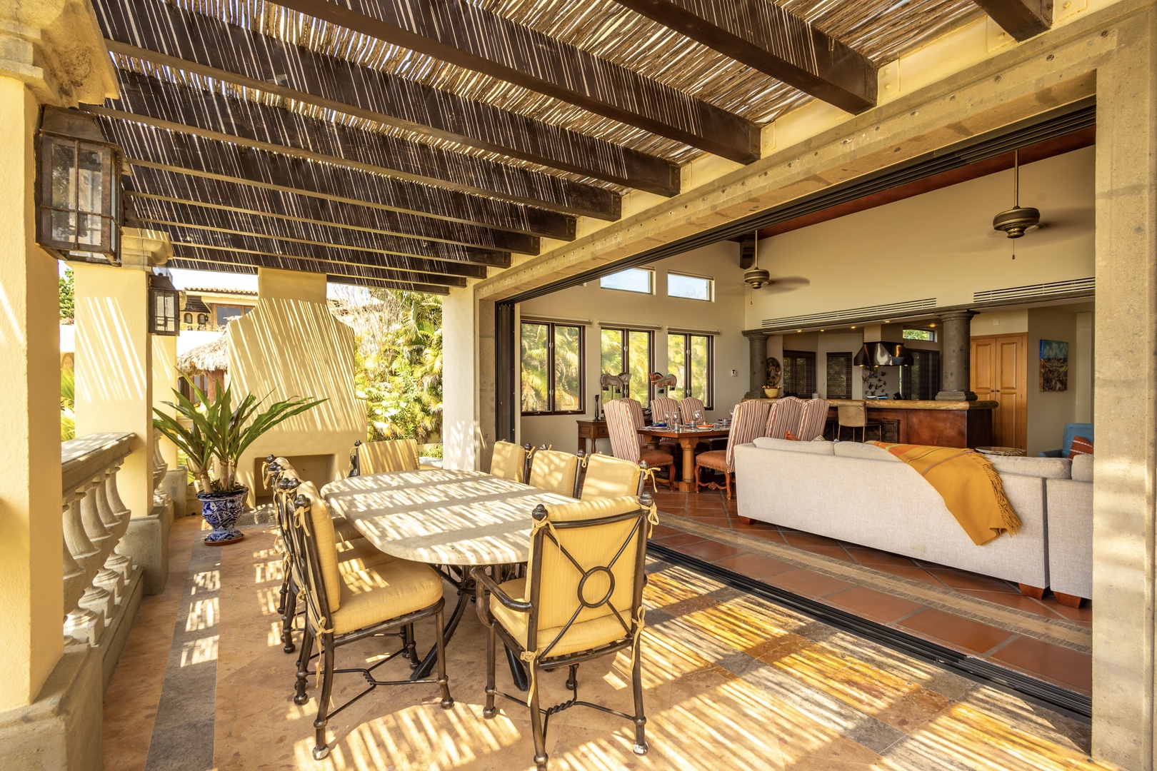 Sunlight streams through the palapa roof, casting beautiful shadows over your outdoor dining space, which flows seamlessly into the open-plan living area—perfect for relaxed indoor-outdoor living.