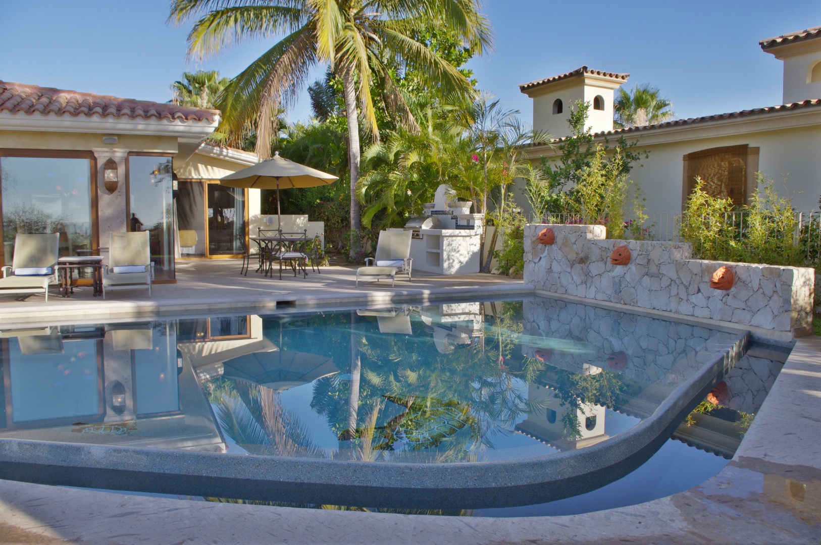 Your private oasis awaits with a stunning pool framed by swaying palms, elegant stone features, and comfortable lounging areas—perfect for soaking up the sun in serene luxury.