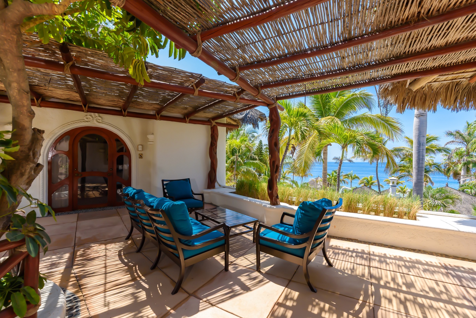 Imagine lounging on this stunning patio, where turquoise cushions invite you to relax under woven shade. Just beyond the palms, sparkling ocean views create your personal paradise for morning coffee or sunset cocktails.
